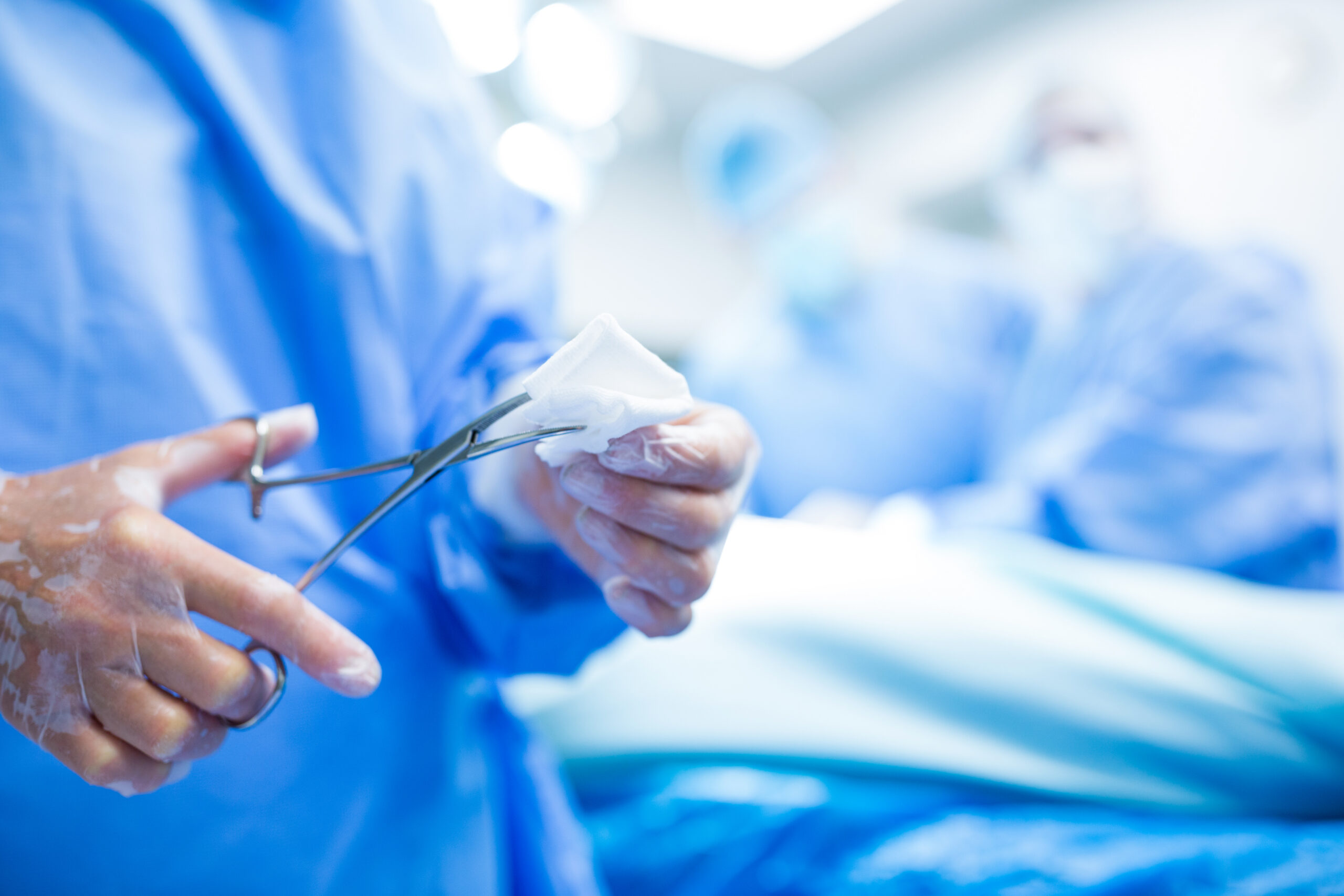 Surgeon cutting cotton from scissor in operation room at hospital