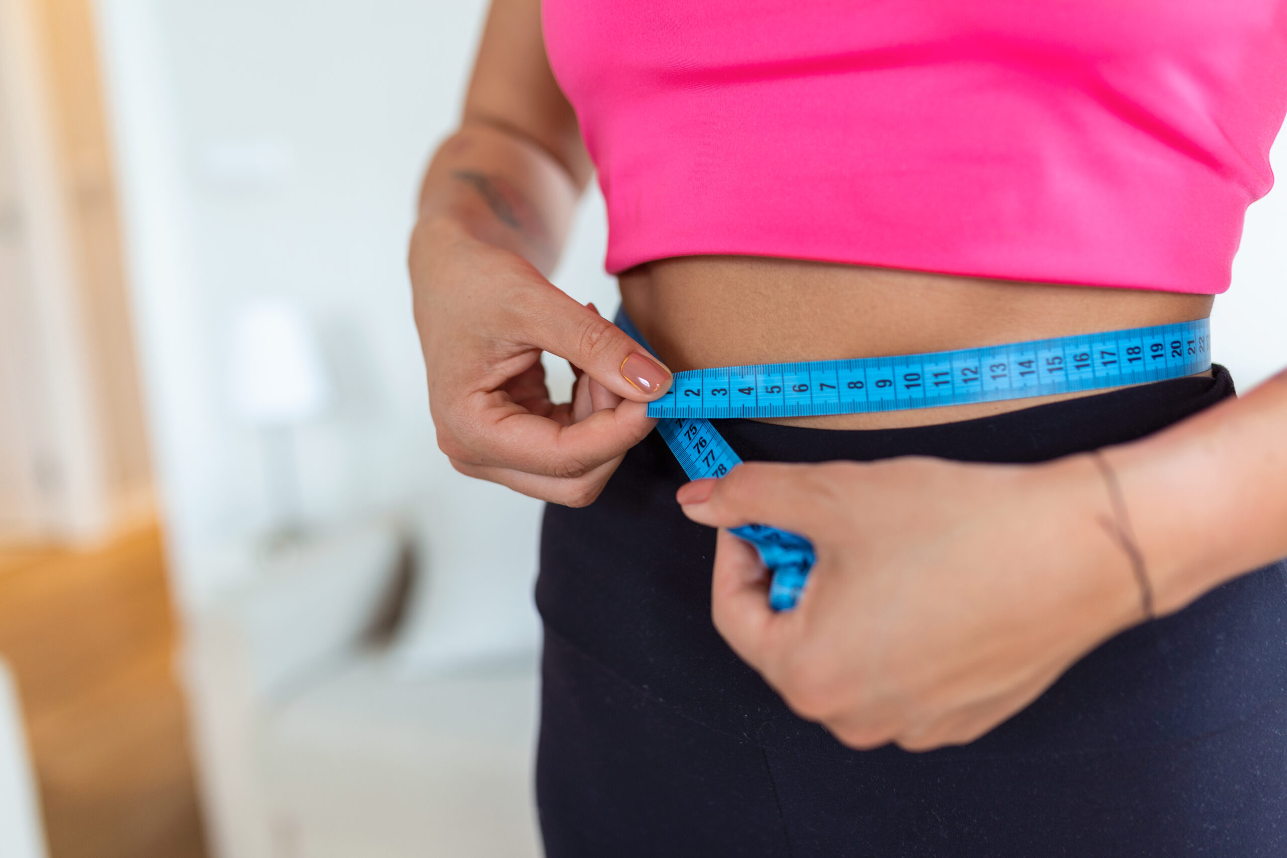 Weight Loss Concept. Portrait of millennial African American lady in top bra and leggings measuring her waist using blue tape, free copy space. Black woman checking body parameters